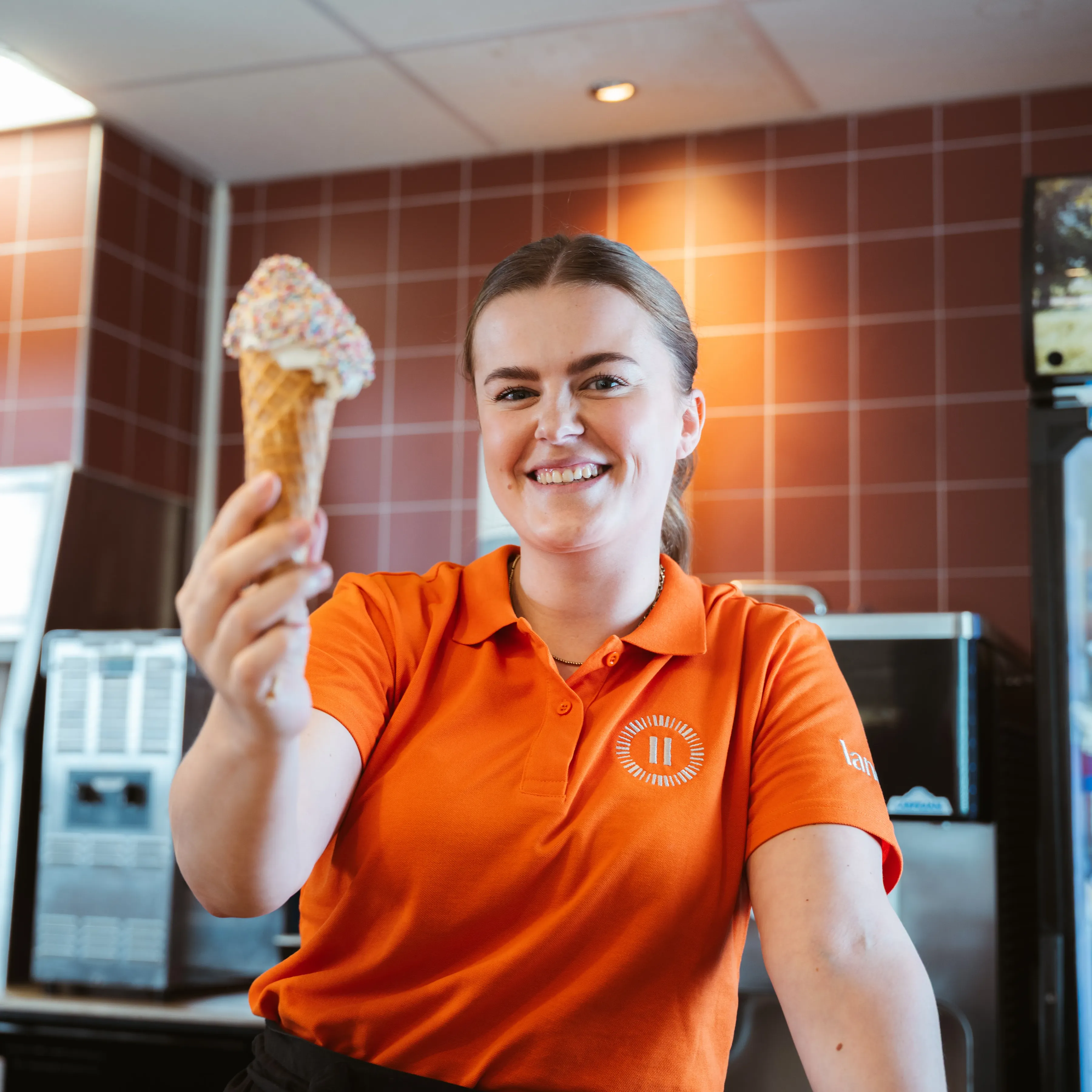 Vrouwelijke medewerker reikt lachend een ijsje aan naar de camera