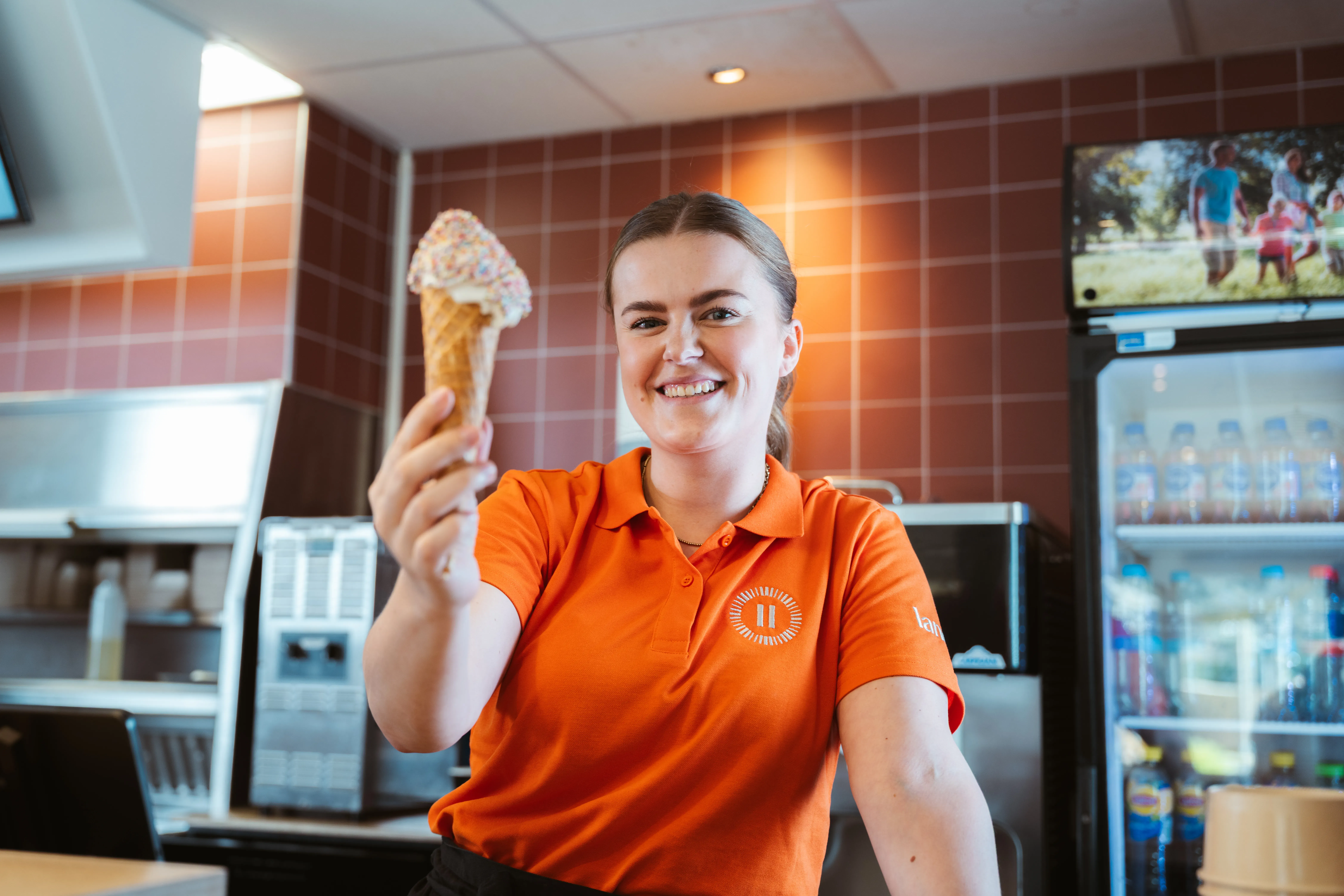 Vrouwelijke medewerker reikt lachend een ijsje aan naar de camera